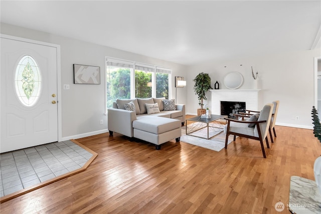 living room with light wood-style floors, a brick fireplace, and baseboards