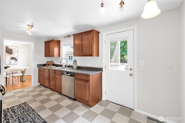kitchen featuring light floors, dishwasher, a sink, dark countertops, and brown cabinetry