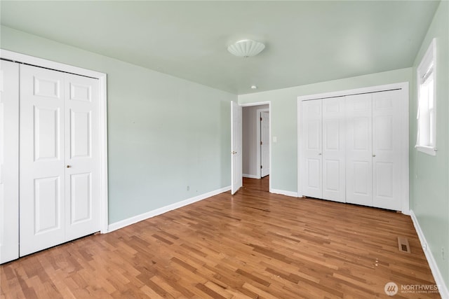 unfurnished bedroom with baseboards, light wood finished floors, and multiple closets