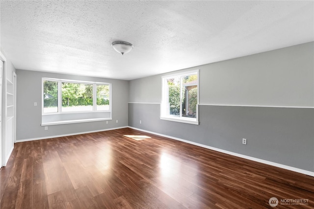 empty room featuring plenty of natural light, a textured ceiling, dark wood-style floors, and baseboards