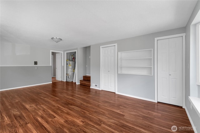 unfurnished living room with water heater, wood finished floors, stairs, and baseboards