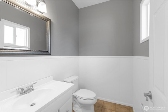 half bathroom with toilet, vanity, and a wainscoted wall