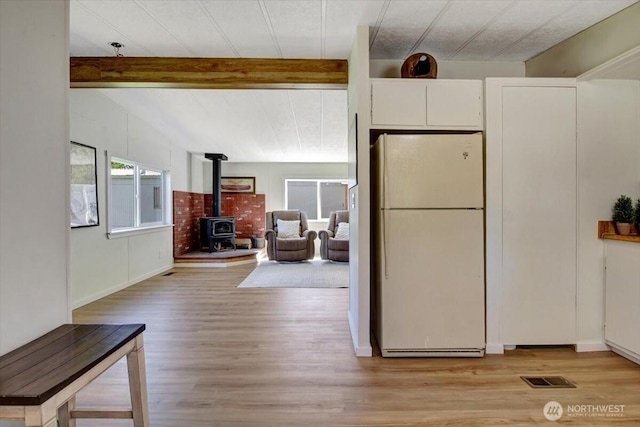 kitchen with freestanding refrigerator, a wood stove, light wood-type flooring, and visible vents