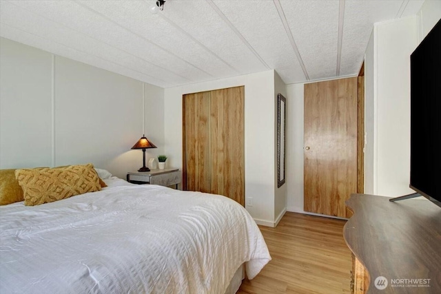 bedroom with baseboards, light wood finished floors, a closet, and a textured ceiling