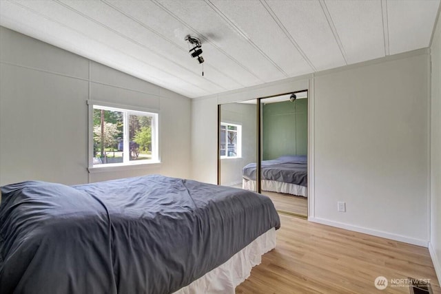 bedroom with vaulted ceiling, a closet, light wood-type flooring, and baseboards