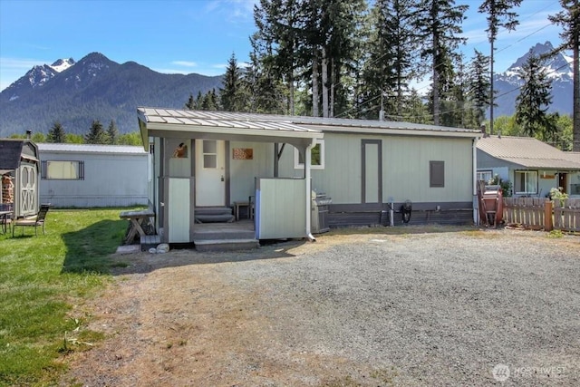 view of front of house featuring a mountain view, fence, metal roof, an outdoor structure, and a front lawn