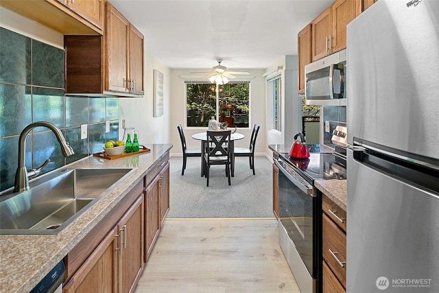 kitchen featuring stainless steel appliances, a sink, brown cabinets, ceiling fan, and light wood-style flooring