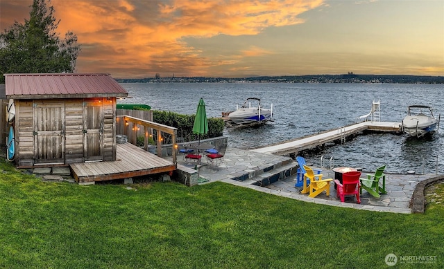 view of dock with a patio, a water view, and a lawn