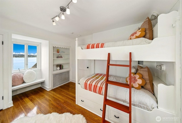 bedroom featuring a water view, wood finished floors, baseboards, and rail lighting