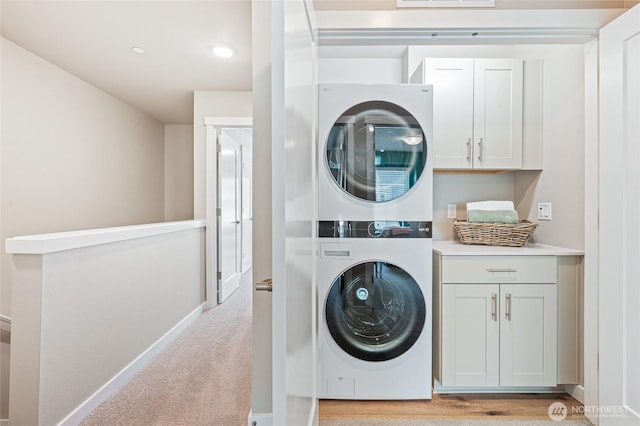 washroom featuring stacked washer and dryer, cabinet space, visible vents, baseboards, and light carpet