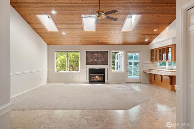 unfurnished living room with wood ceiling, a sink, a lit fireplace, a skylight, and light carpet