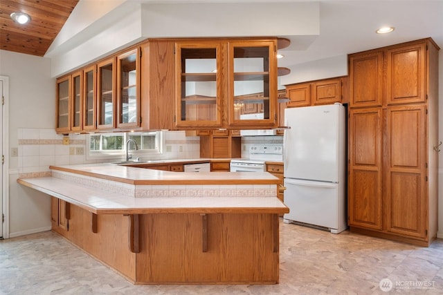 kitchen with brown cabinetry, white appliances, light countertops, and a sink