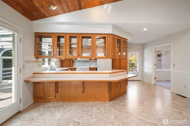 kitchen featuring a sink, a peninsula, lofted ceiling, white appliances, and glass insert cabinets