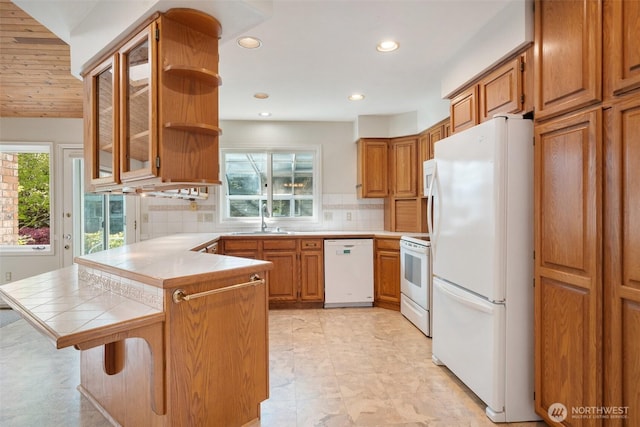 kitchen with a peninsula, a sink, open shelves, white appliances, and tile countertops