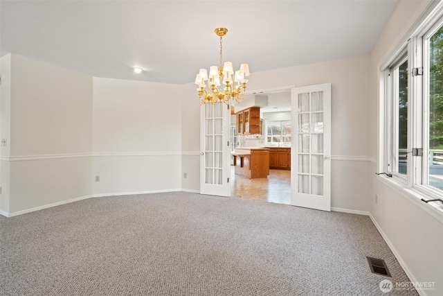 spare room with an inviting chandelier, french doors, visible vents, baseboards, and light colored carpet