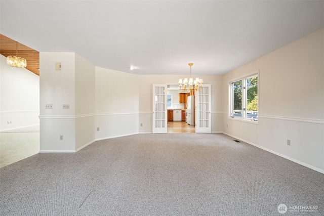 spare room with baseboards, french doors, a chandelier, and light colored carpet
