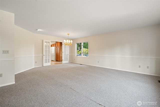 empty room with an inviting chandelier, carpet floors, and baseboards