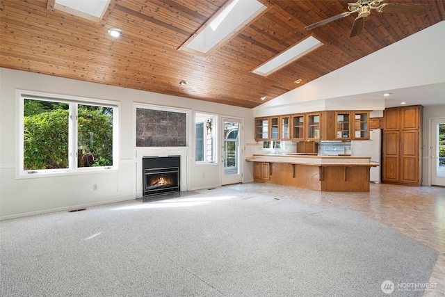 unfurnished living room with a healthy amount of sunlight, wood ceiling, a fireplace with flush hearth, and visible vents