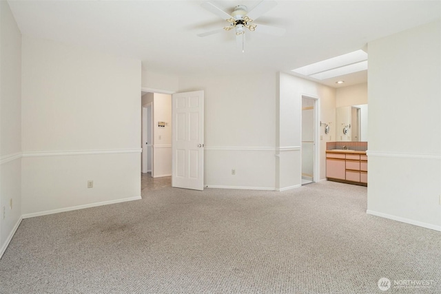 spare room with a skylight, light carpet, baseboards, and a ceiling fan