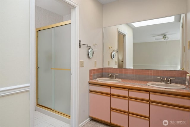 bathroom featuring double vanity, a stall shower, a skylight, and a sink