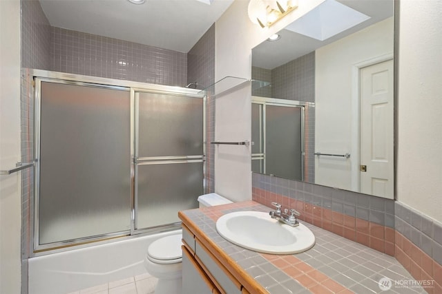 bathroom with a skylight, toilet, vanity, backsplash, and enclosed tub / shower combo