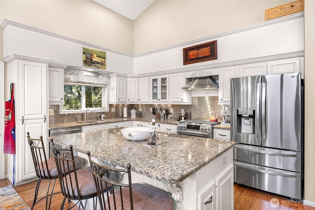 6874 Golf View Dr, Lynden, WA 98264 - kitchen with stainless steel appliances, a sink, a breakfast bar area, wall chimney exhaust hood, and tasteful backsplash