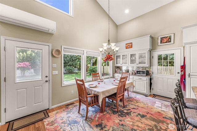 6874 Golf View Dr, Lynden, WA 98264 - dining room with high vaulted ceiling, a wall unit AC, a chandelier, light wood-type flooring, and baseboards
