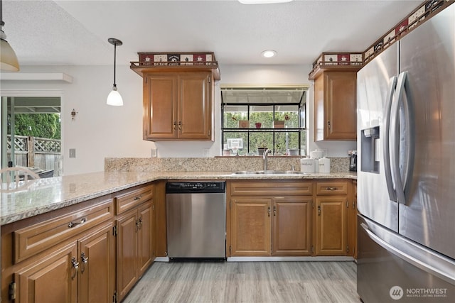 kitchen with appliances with stainless steel finishes, a sink, light wood-type flooring, brown cabinetry, and a textured ceiling