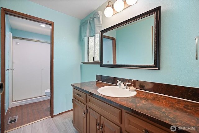 full bathroom with toilet, vanity, a stall shower, and wood finished floors