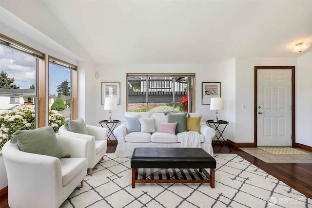living area with healthy amount of natural light, light wood finished floors, baseboards, and vaulted ceiling