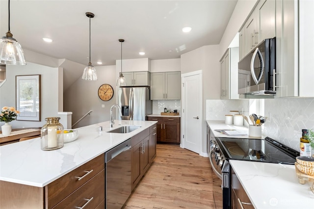 kitchen with a sink, stainless steel appliances, a center island with sink, light wood-style flooring, and light stone countertops