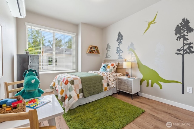 bedroom with wood finished floors, baseboards, and a wall unit AC