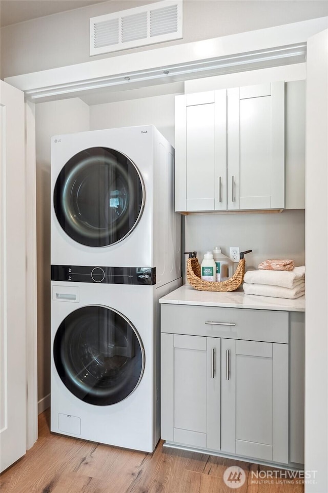 clothes washing area featuring cabinet space, light wood-style flooring, stacked washer and dryer, and visible vents
