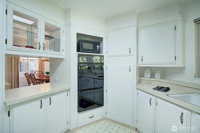 kitchen with glass insert cabinets, a sink, white cabinetry, black appliances, and light countertops