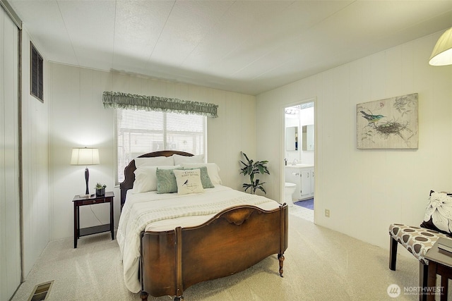 bedroom with ensuite bathroom, visible vents, and light colored carpet