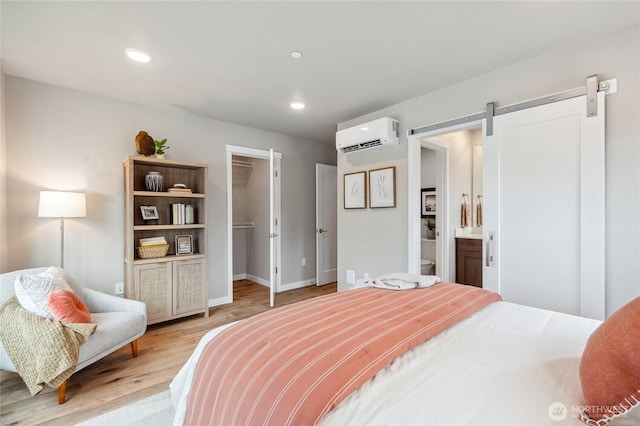 bedroom featuring light wood finished floors, a wall unit AC, a barn door, a spacious closet, and recessed lighting