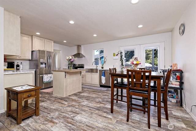 kitchen with stainless steel appliances, wall chimney range hood, wood finished floors, recessed lighting, and a textured ceiling