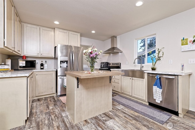 kitchen with stainless steel appliances, wall chimney exhaust hood, a sink, light countertops, and wood finished floors
