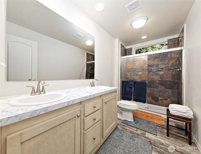 full bath with double vanity, a stall shower, toilet, and wood finished floors