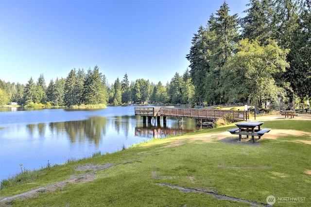 dock area with a lawn, a water view, and a view of trees