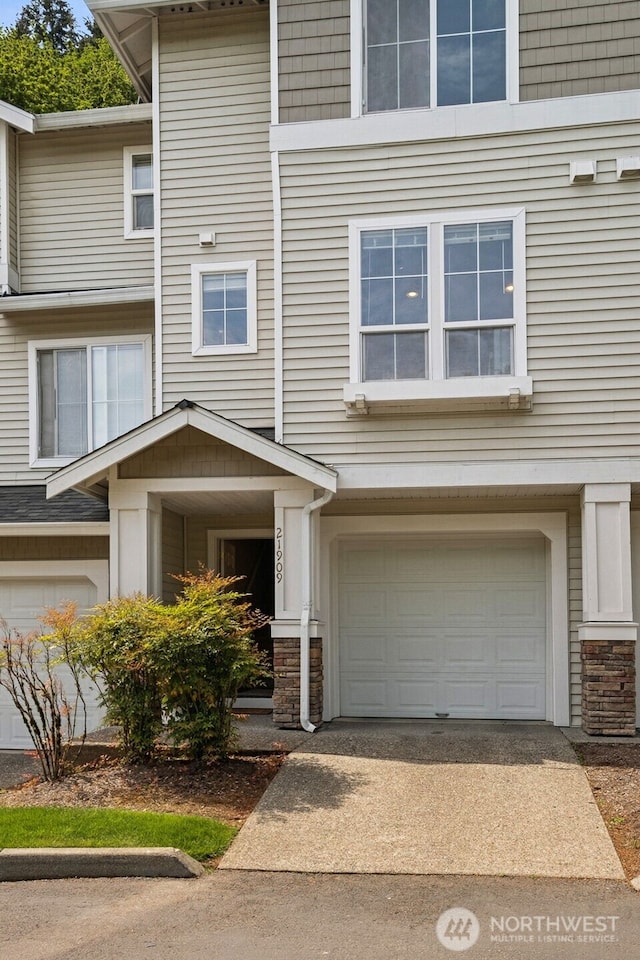 multi unit property featuring a garage, driveway, and stone siding