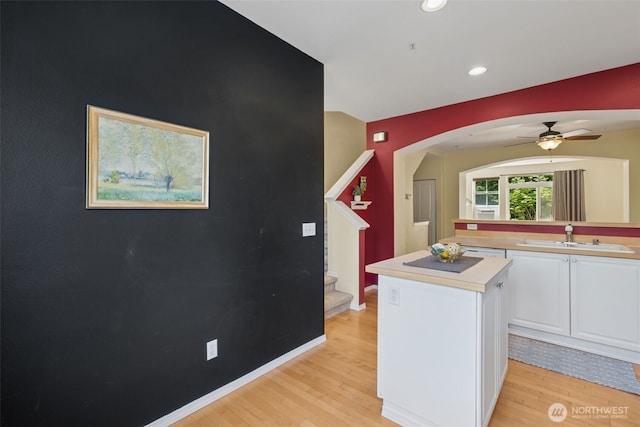 kitchen featuring a sink, white cabinets, light countertops, a center island, and light wood finished floors