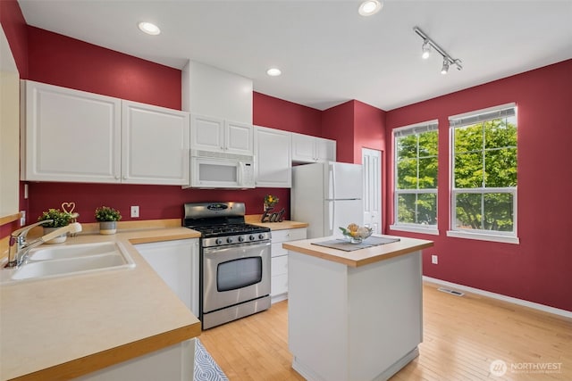 kitchen featuring white appliances, a sink, light countertops, and white cabinetry