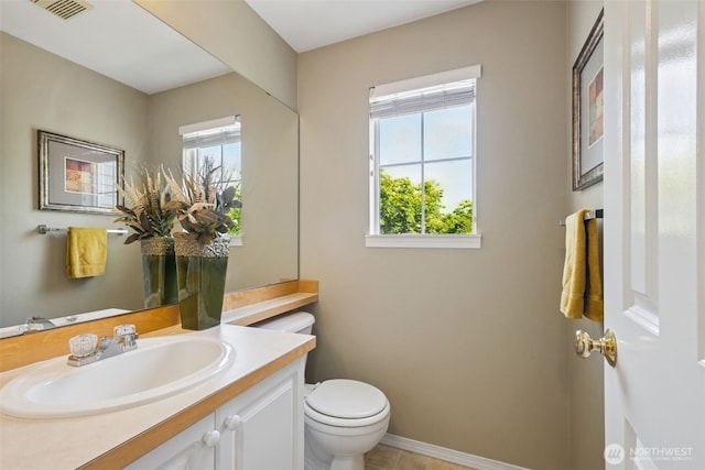 bathroom with toilet, plenty of natural light, vanity, and baseboards