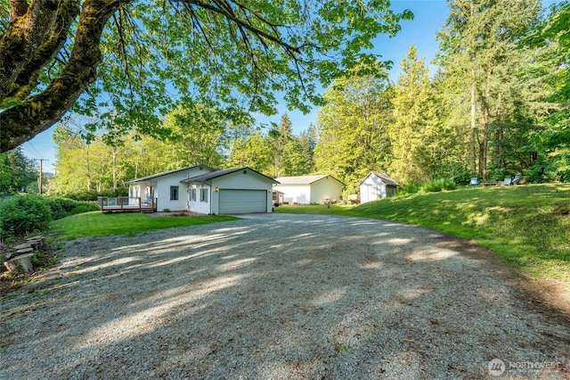 view of front of property featuring an attached garage, gravel driveway, a front lawn, and a wooden deck