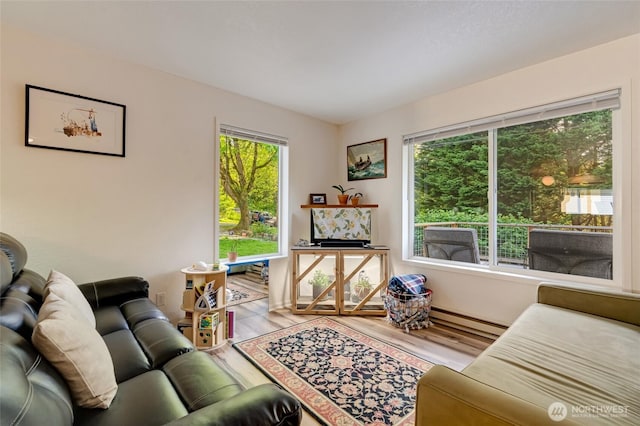 living area featuring healthy amount of natural light, wood finished floors, and a baseboard heating unit