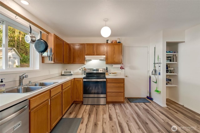 kitchen featuring stainless steel appliances, under cabinet range hood, a sink, light wood finished floors, and light countertops
