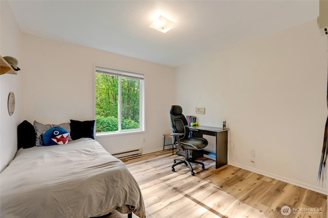 bedroom with a baseboard radiator, light wood-style floors, baseboards, and a desk