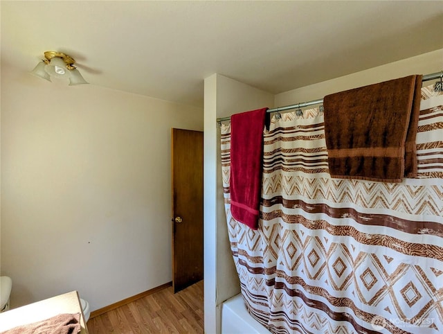 bathroom with wood finished floors, toilet, baseboards, and shower / bath combo with shower curtain