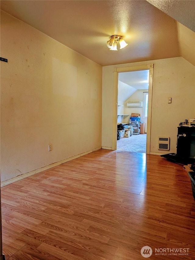 unfurnished dining area featuring light wood finished floors, a wall unit AC, lofted ceiling, and heating unit